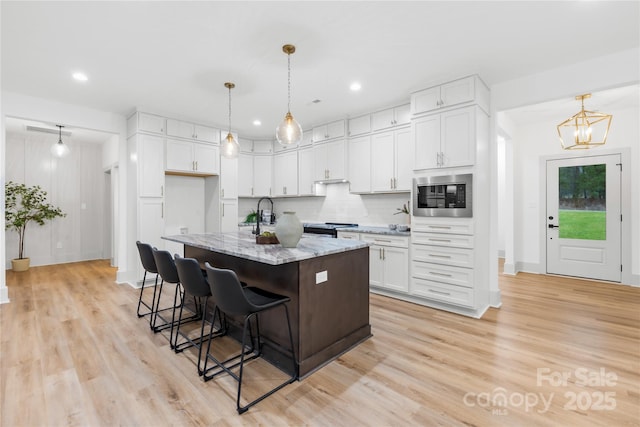 5147 Star Magnolia Ct, Clover, SC 29710 - kitchen featuring a breakfast bar, appliances with stainless steel finishes, white cabinetry, light wood-type flooring, and light stone counters