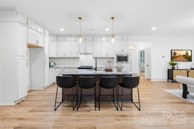 5147 Star Magnolia Ct, Clover, SC 29710 - kitchen featuring white cabinetry, a breakfast bar area, light wood-type flooring, stainless steel appliances, and decorative backsplash