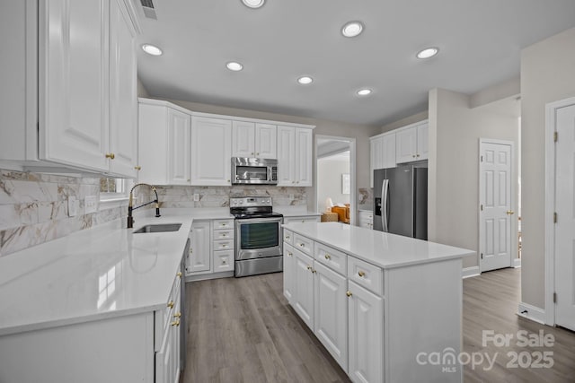 kitchen featuring white cabinetry, stainless steel appliances, a kitchen island, sink, and tasteful backsplash