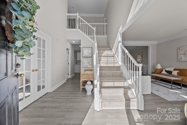 entryway featuring a high ceiling, french doors, crown molding, and light hardwood / wood-style floors