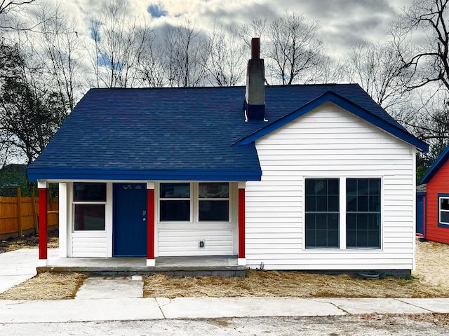 view of front of house with a chimney, fence, and roof with shingles