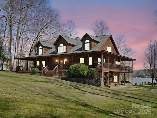 back of house at dusk with covered porch, a water view, a yard, and a patio