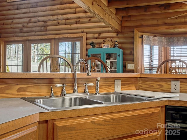 kitchen with a sink, brown cabinetry, log walls, and light countertops