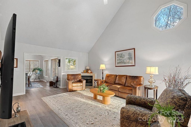 living room with baseboards, high vaulted ceiling, wood finished floors, and a tile fireplace