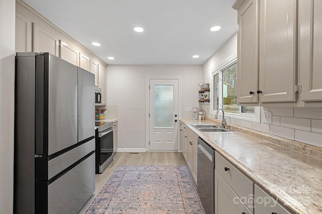 kitchen featuring stainless steel appliances, light countertops, decorative backsplash, light wood-style floors, and a sink