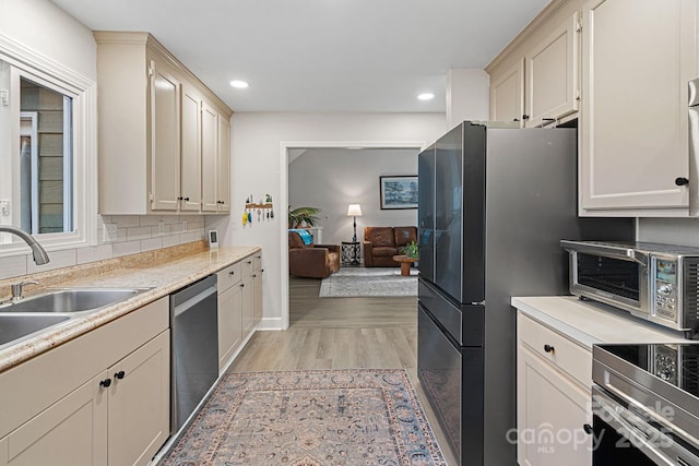 kitchen featuring decorative backsplash, appliances with stainless steel finishes, light countertops, light wood-type flooring, and a sink