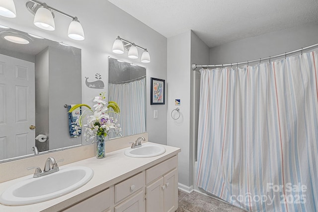 full bathroom with a textured ceiling, double vanity, a sink, and baseboards