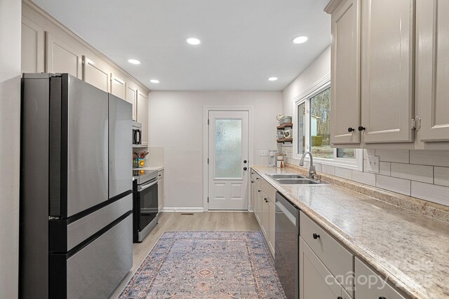 kitchen featuring stainless steel appliances, a sink, decorative backsplash, light countertops, and light wood-type flooring