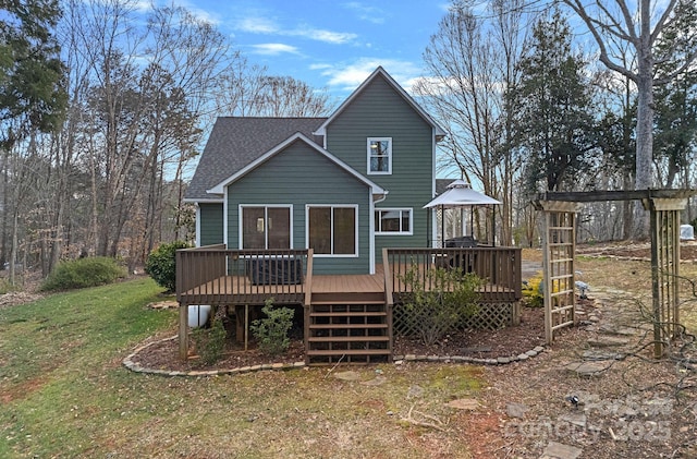 back of property with a yard, roof with shingles, and a wooden deck