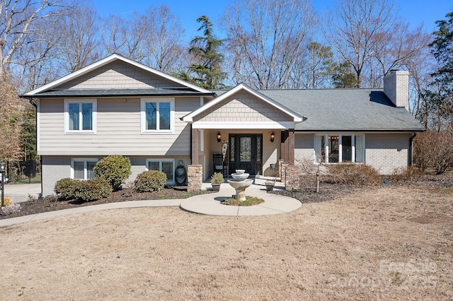 tri-level home featuring a shingled roof, a chimney, central AC, and brick siding