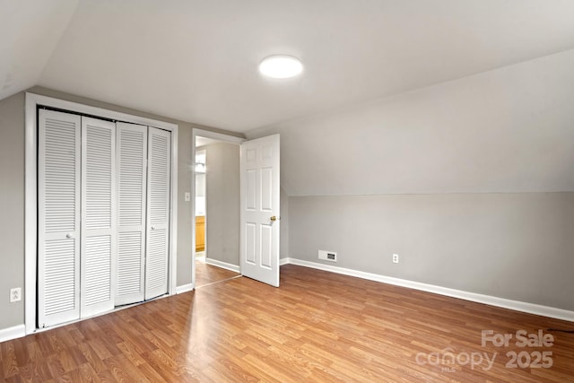 unfurnished bedroom featuring light wood-type flooring, a closet, and lofted ceiling