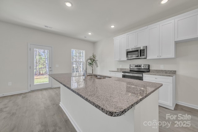 kitchen with stainless steel appliances, light wood-style floors, a sink, and light stone countertops