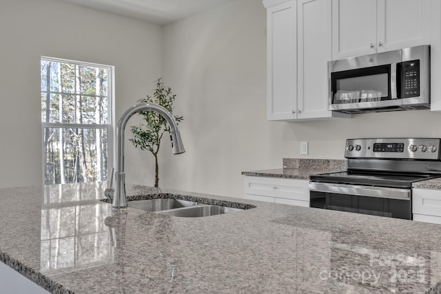 kitchen featuring stainless steel appliances, white cabinetry, a sink, and light stone counters