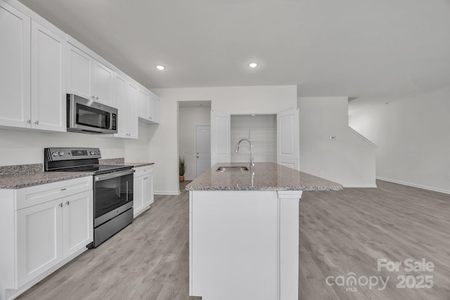 kitchen with appliances with stainless steel finishes, light wood-style flooring, a sink, and light stone counters