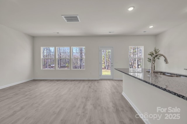 unfurnished living room featuring light wood finished floors, baseboards, visible vents, a sink, and recessed lighting