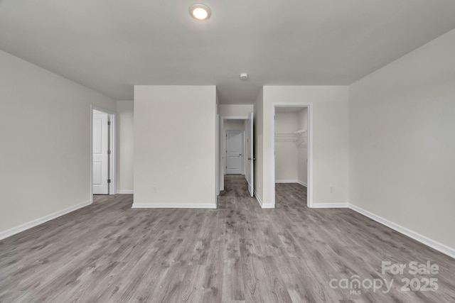 unfurnished bedroom featuring a spacious closet, a closet, wood finished floors, and baseboards