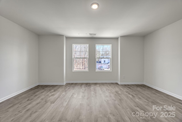 empty room with wood finished floors, visible vents, and baseboards