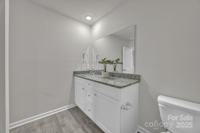 bathroom featuring toilet, baseboards, wood finished floors, and vanity