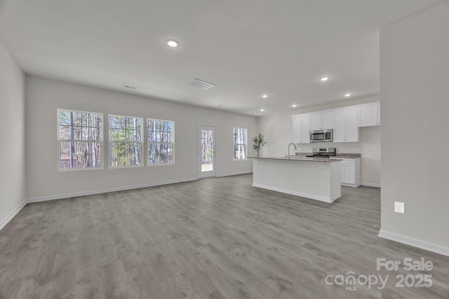 kitchen with appliances with stainless steel finishes, light wood-style floors, open floor plan, white cabinetry, and baseboards