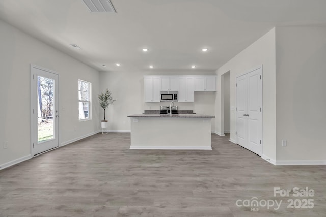 kitchen featuring dark countertops, stainless steel microwave, visible vents, white cabinets, and light wood-type flooring