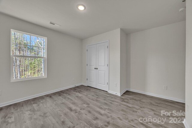 unfurnished bedroom with a closet, wood finished floors, visible vents, and baseboards