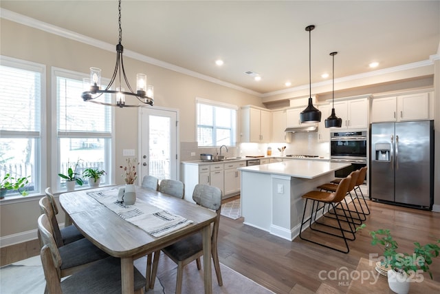 dining room featuring an inviting chandelier, ornamental molding, sink, and dark wood-type flooring