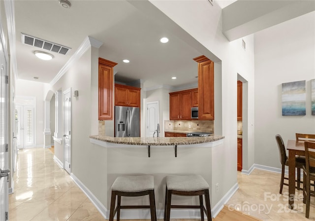 kitchen with ornamental molding, appliances with stainless steel finishes, a breakfast bar area, and decorative backsplash