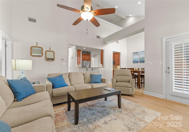 living room with a towering ceiling, light hardwood / wood-style flooring, and ceiling fan