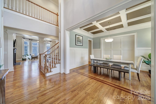 dining room with coffered ceiling, stairs, decorative columns, crown molding, and light wood-style flooring