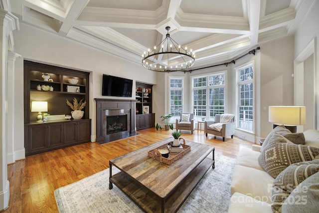 living room with coffered ceiling, beam ceiling, light wood-type flooring, a high end fireplace, and an inviting chandelier