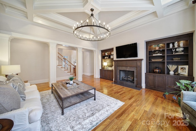 living area with coffered ceiling, decorative columns, light wood-style floors, and a premium fireplace