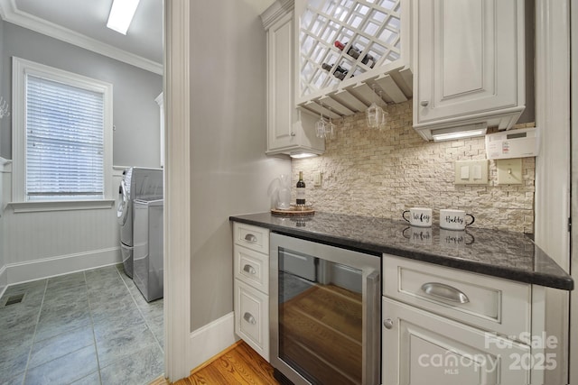 bar with a wainscoted wall, crown molding, a dry bar, washer and dryer, and beverage cooler