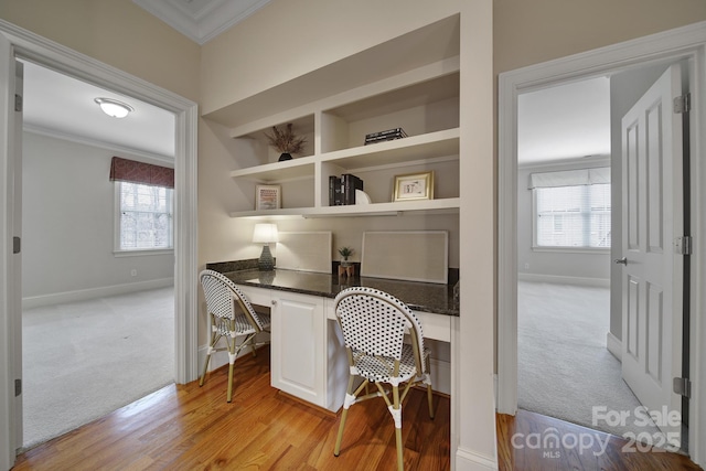 office area with light colored carpet, built in desk, baseboards, and ornamental molding