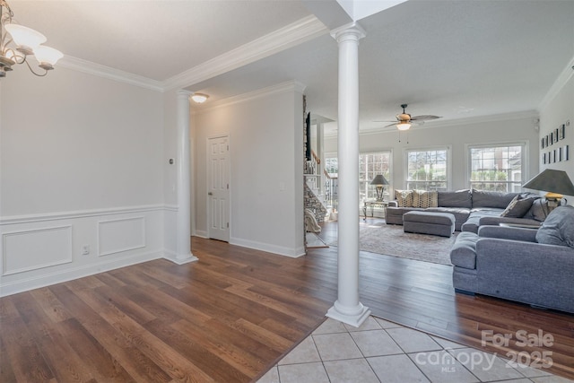 living room featuring wood-type flooring, crown molding, decorative columns, and ceiling fan with notable chandelier