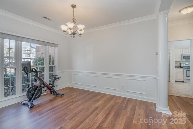 workout area featuring a notable chandelier, light hardwood / wood-style floors, crown molding, and ornate columns