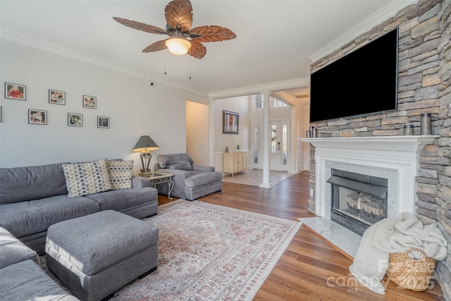 living room with ceiling fan, crown molding, a stone fireplace, and wood-type flooring