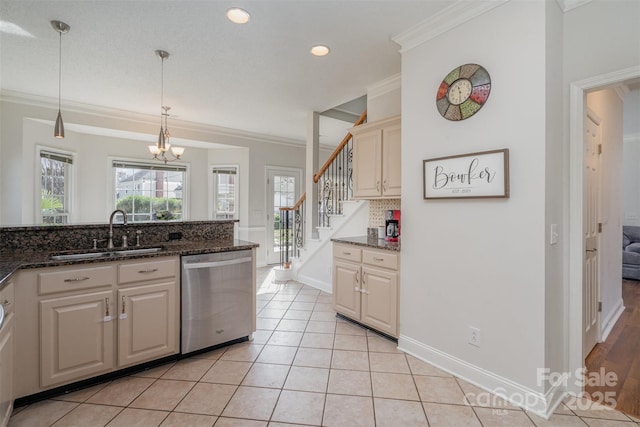 kitchen with stainless steel dishwasher, decorative light fixtures, ornamental molding, sink, and dark stone countertops