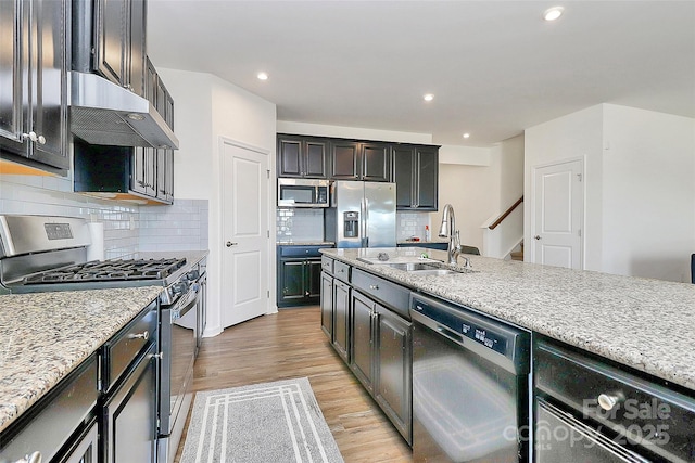 kitchen featuring under cabinet range hood, stainless steel appliances, a sink, light wood-type flooring, and tasteful backsplash