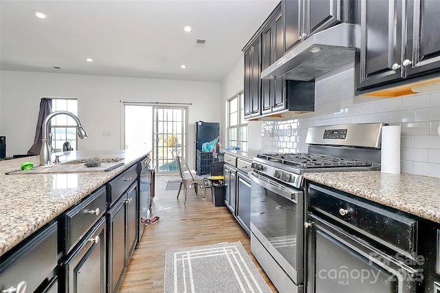 kitchen featuring light wood finished floors, visible vents, a sink, stainless steel gas range, and under cabinet range hood