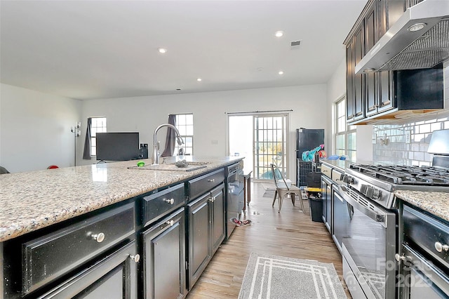 kitchen featuring stainless steel appliances, light wood-style floors, a sink, wall chimney range hood, and light stone countertops