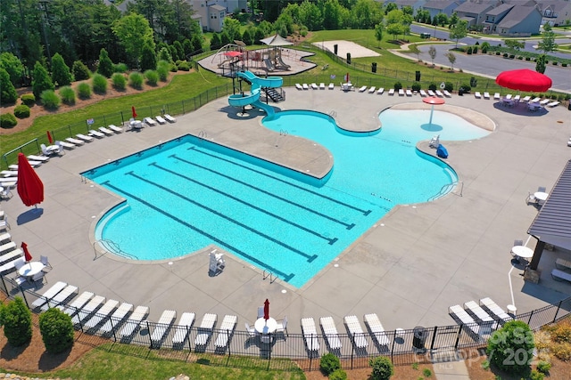 community pool with a yard, a water slide, a patio area, and fence