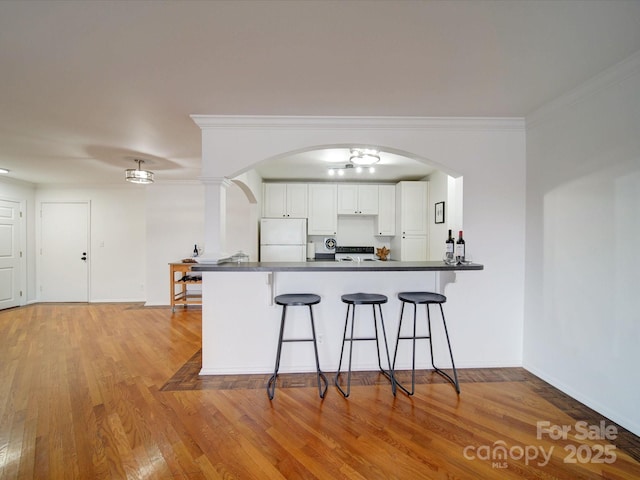 kitchen with dark countertops, freestanding refrigerator, a peninsula, a kitchen bar, and white cabinetry