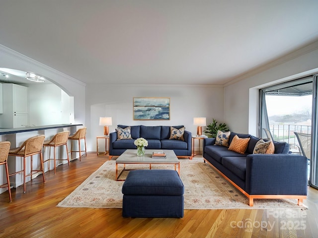 living room featuring wood finished floors, arched walkways, and crown molding