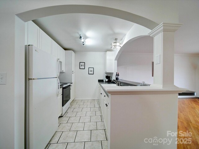 kitchen featuring a sink, arched walkways, freestanding refrigerator, electric range, and white cabinetry