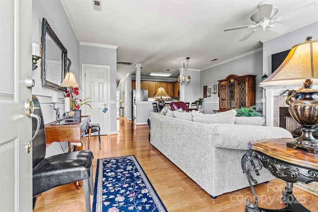 living area with visible vents, a tile fireplace, ornamental molding, light wood-type flooring, and ceiling fan with notable chandelier