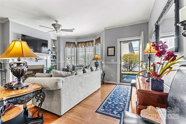 living room with baseboards, ceiling fan, ornamental molding, light wood-style floors, and a fireplace