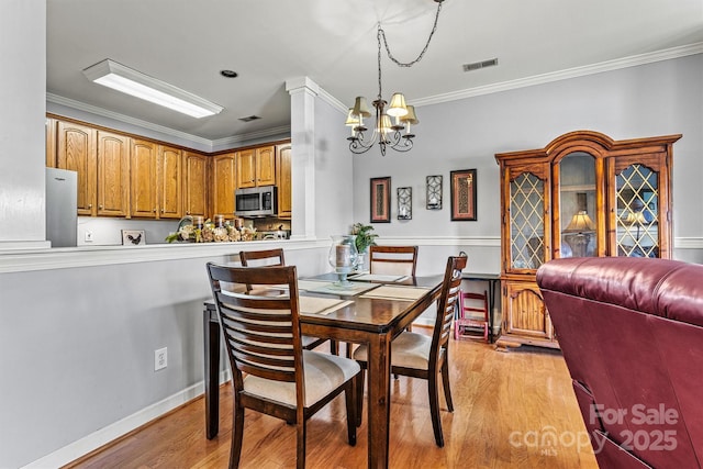 dining space featuring visible vents, baseboards, crown molding, light wood-style floors, and a chandelier