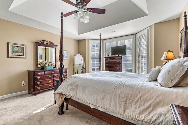 bedroom featuring a tray ceiling, light colored carpet, visible vents, a ceiling fan, and baseboards