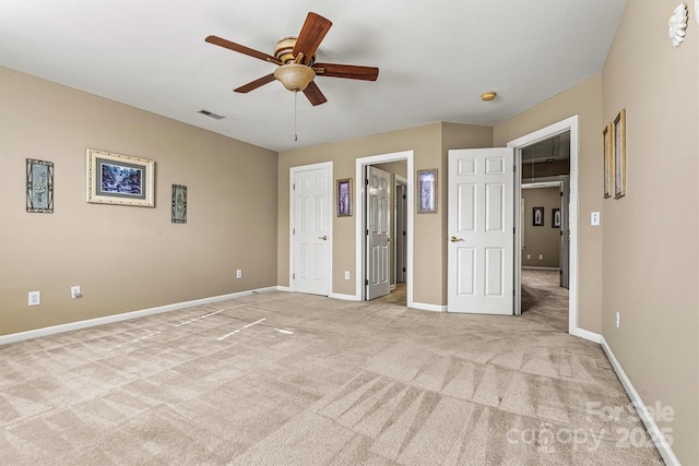 unfurnished bedroom featuring light colored carpet, visible vents, ensuite bathroom, ceiling fan, and baseboards