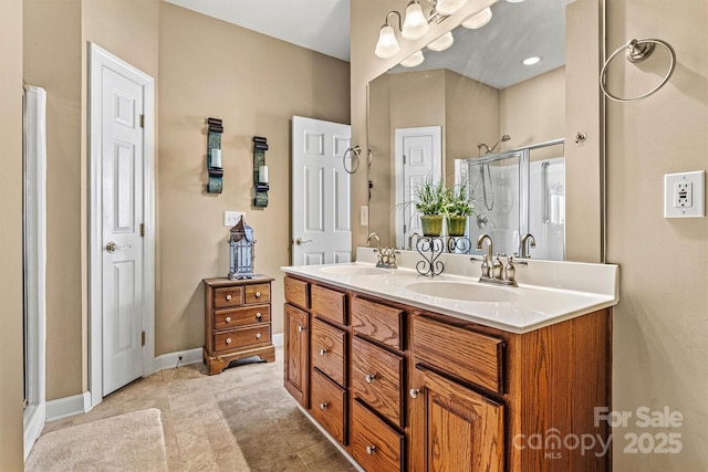 full bath with double vanity, a stall shower, baseboards, and a sink